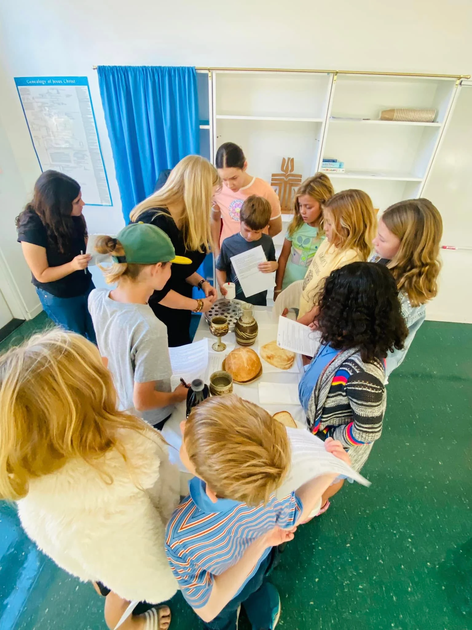 Children and their teachers gathered around a table set with bread and a cup for one of our lessons.