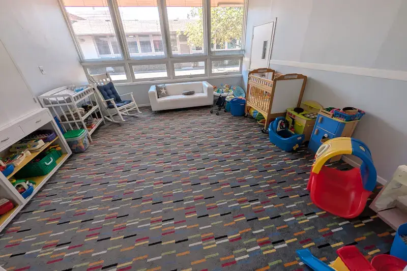 The Sunday nursery: a crib, a small slide, a toy kitchen, and a rocking chair under the windows